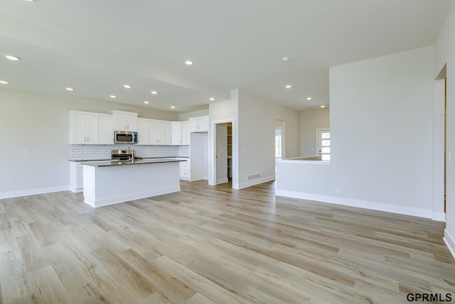 kitchen featuring white cabinetry, open floor plan, appliances with stainless steel finishes, decorative backsplash, and light wood finished floors