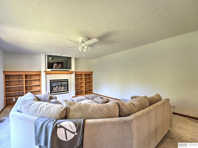 living room featuring ceiling fan, a tiled fireplace, light carpet, and a textured ceiling