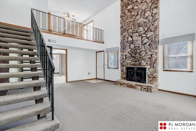 unfurnished living room featuring a stone fireplace, carpet floors, ceiling fan, and a towering ceiling