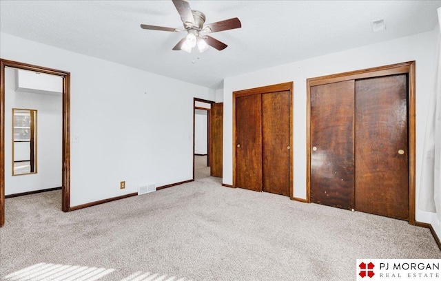 unfurnished bedroom featuring multiple closets, ceiling fan, light carpet, and a textured ceiling