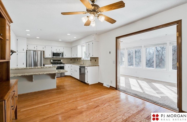 kitchen featuring a breakfast bar, appliances with stainless steel finishes, kitchen peninsula, light stone countertops, and white cabinets