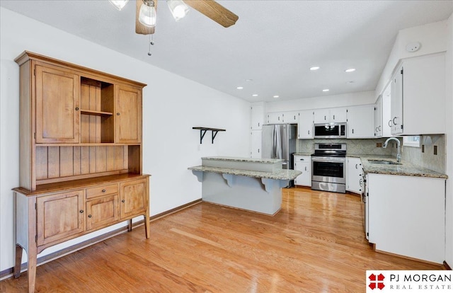 kitchen with sink, white cabinetry, appliances with stainless steel finishes, light hardwood / wood-style floors, and backsplash