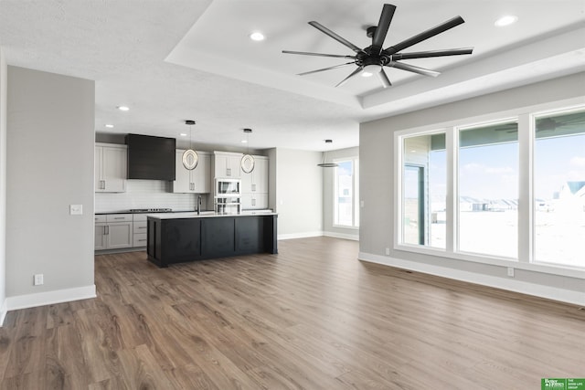 kitchen featuring open floor plan, ventilation hood, tasteful backsplash, stainless steel microwave, and a raised ceiling