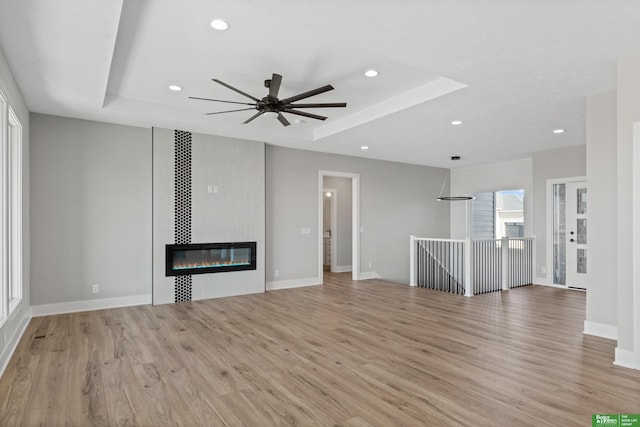 unfurnished living room with a tile fireplace, recessed lighting, wood finished floors, baseboards, and a tray ceiling