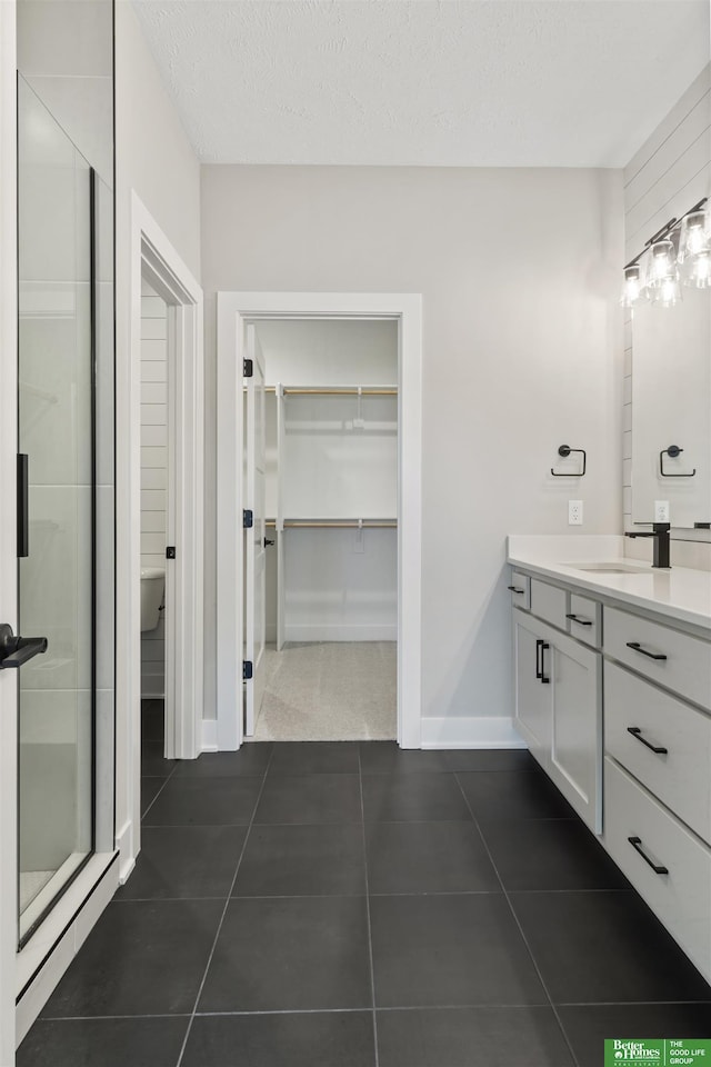 bathroom featuring a textured ceiling, vanity, tile patterned floors, a stall shower, and a walk in closet