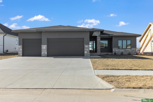 prairie-style house featuring a garage, stone siding, a front lawn, and concrete driveway