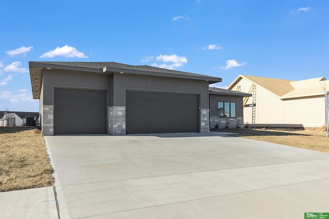 prairie-style home featuring stone siding, central AC, driveway, and an attached garage