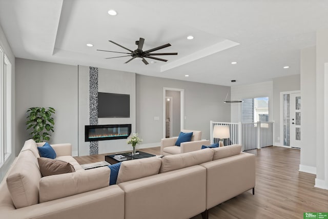 living room with light wood-style floors, a tray ceiling, a fireplace, and recessed lighting