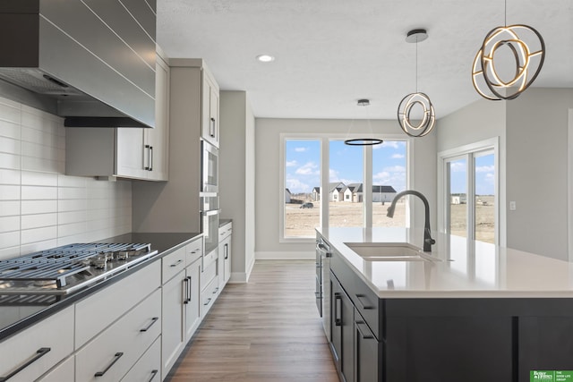 kitchen featuring tasteful backsplash, custom range hood, appliances with stainless steel finishes, a kitchen island with sink, and a sink