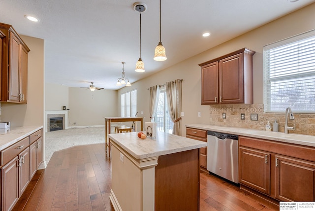 kitchen featuring open floor plan, a center island, light countertops, pendant lighting, and stainless steel dishwasher