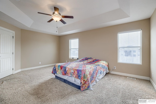 bedroom with baseboards, visible vents, a ceiling fan, carpet, and a tray ceiling