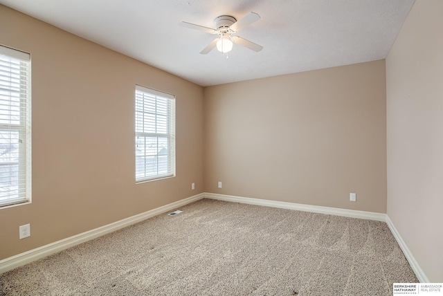 carpeted empty room with ceiling fan, visible vents, a wealth of natural light, and baseboards