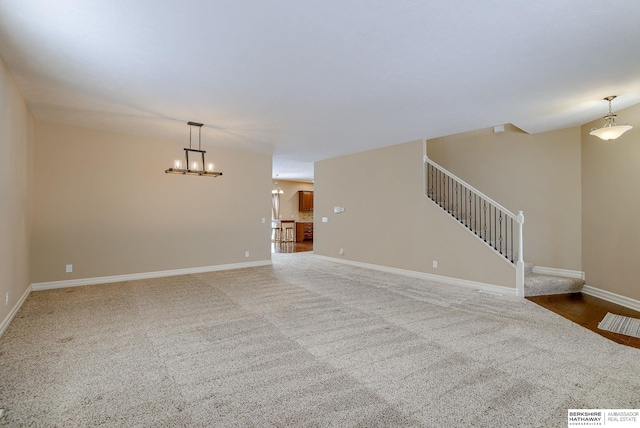 unfurnished living room with a chandelier, carpet floors, baseboards, and stairs