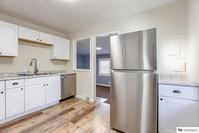 kitchen featuring sink, white cabinetry, light stone counters, appliances with stainless steel finishes, and light hardwood / wood-style floors