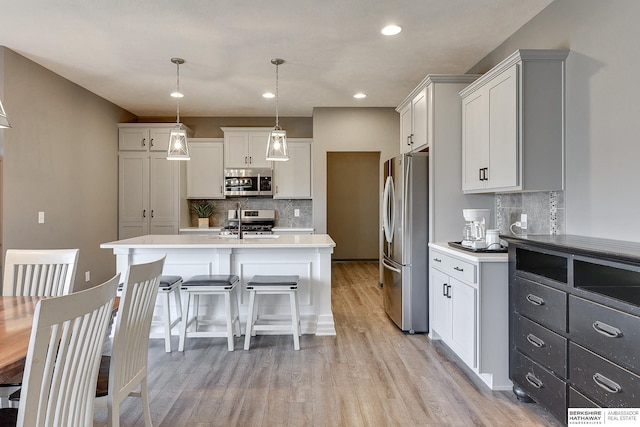 kitchen with appliances with stainless steel finishes, white cabinets, a center island with sink, decorative light fixtures, and light wood-type flooring