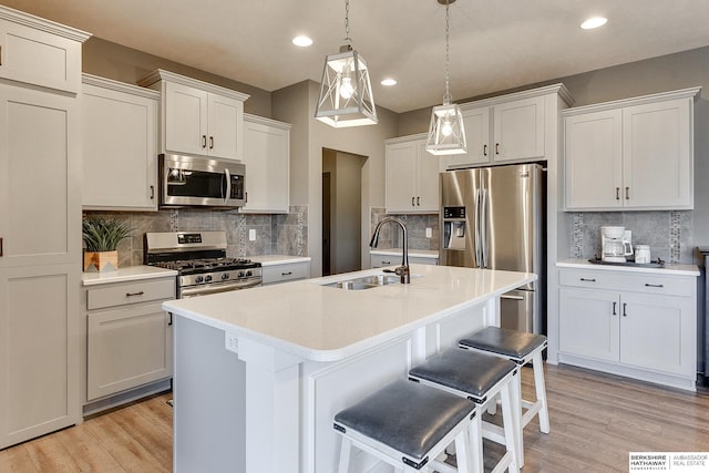 kitchen with sink, appliances with stainless steel finishes, a kitchen island with sink, white cabinets, and decorative light fixtures