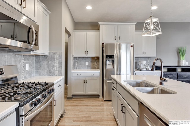 kitchen featuring decorative light fixtures, sink, white cabinets, stainless steel appliances, and light hardwood / wood-style flooring