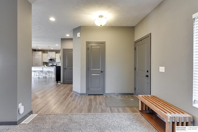 hallway with light hardwood / wood-style floors and a textured ceiling