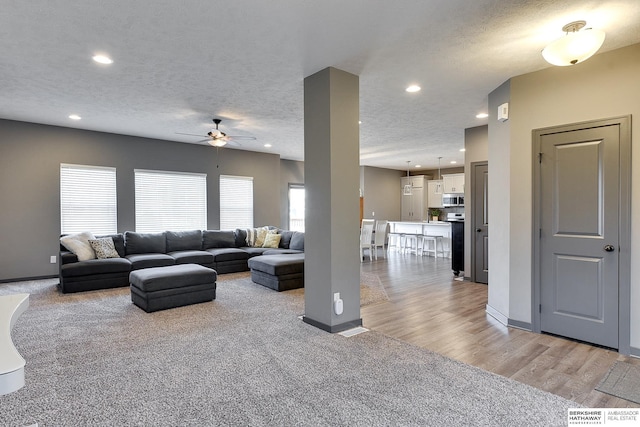 living room with ceiling fan, plenty of natural light, light wood-type flooring, and a textured ceiling