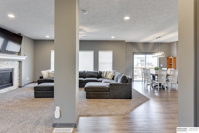 living room with ceiling fan, a stone fireplace, wood-type flooring, and a textured ceiling