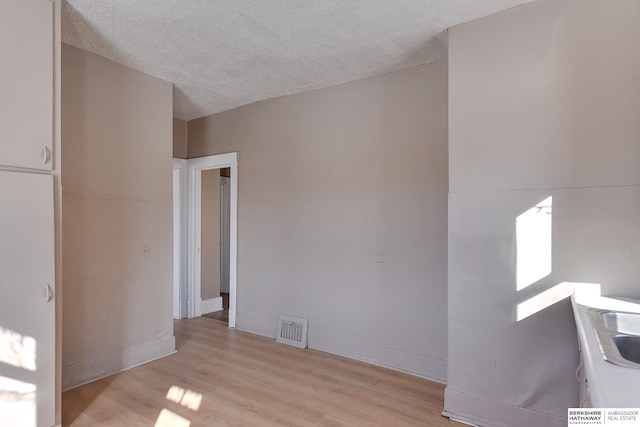 unfurnished room with baseboards, light wood-style flooring, visible vents, and a textured ceiling