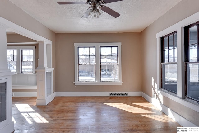 unfurnished dining area featuring decorative columns, visible vents, a textured ceiling, light wood-type flooring, and baseboards