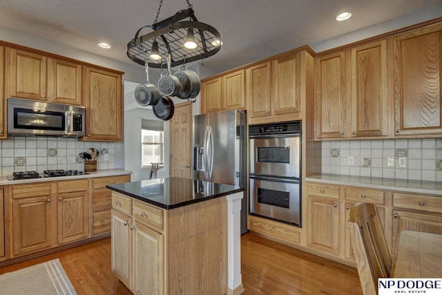 kitchen with appliances with stainless steel finishes, decorative light fixtures, tasteful backsplash, a center island, and light hardwood / wood-style floors