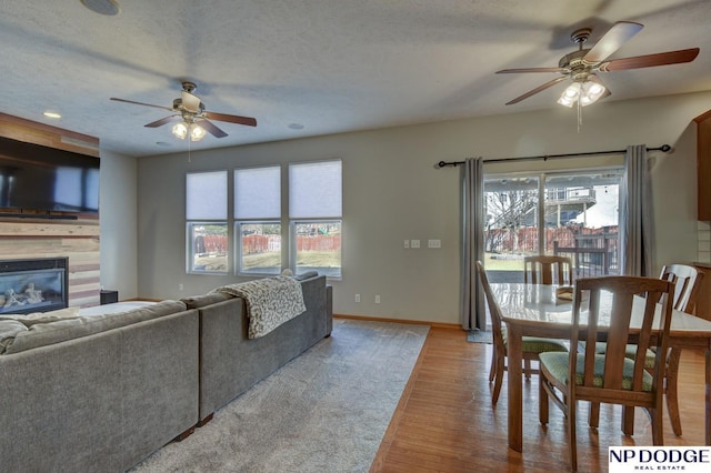 living room featuring ceiling fan, light hardwood / wood-style floors, a tile fireplace, and a textured ceiling