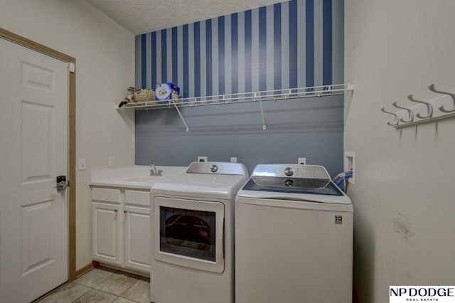 clothes washing area featuring sink, cabinets, washer and dryer, light tile patterned floors, and a textured ceiling