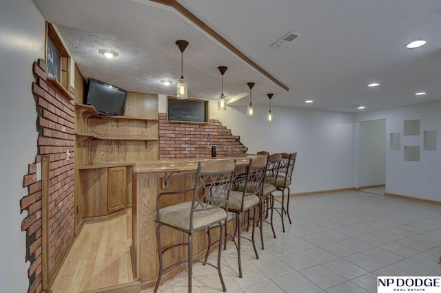 bar with decorative light fixtures, a textured ceiling, and light tile patterned flooring