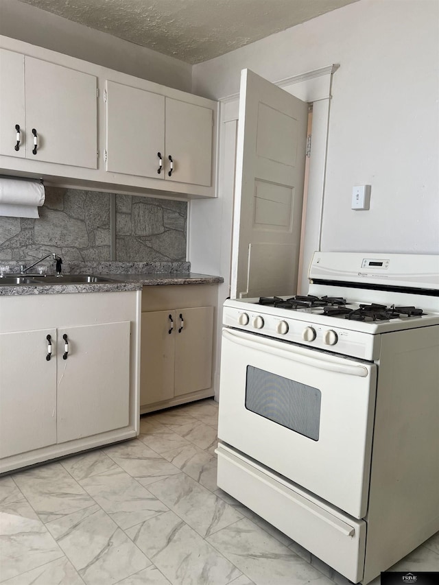 kitchen featuring marble finish floor, white gas stove, backsplash, a sink, and a textured ceiling