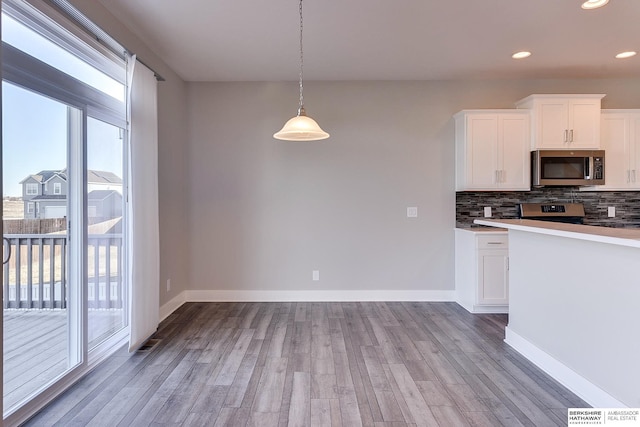 kitchen with pendant lighting, tasteful backsplash, white cabinetry, stainless steel appliances, and light hardwood / wood-style flooring