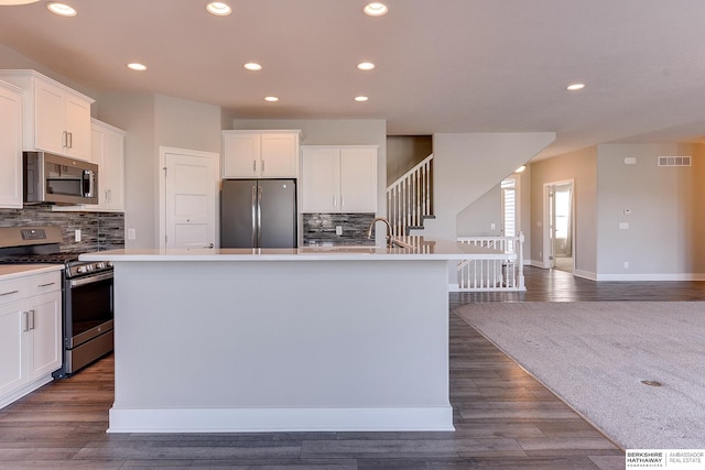 kitchen with tasteful backsplash, appliances with stainless steel finishes, dark hardwood / wood-style flooring, a kitchen island with sink, and white cabinets