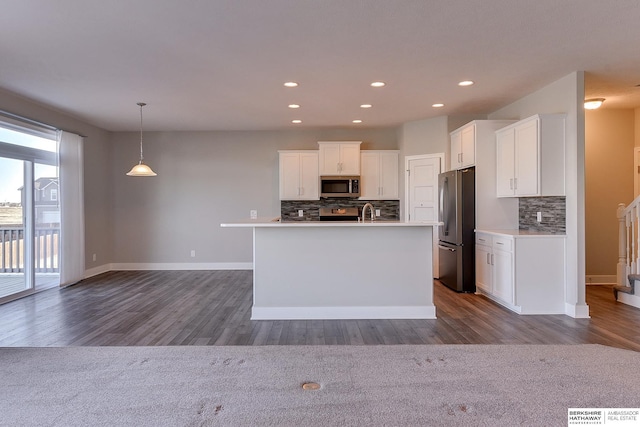 kitchen featuring pendant lighting, stainless steel appliances, white cabinets, and a center island with sink