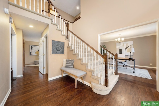 stairway featuring crown molding, a notable chandelier, hardwood / wood-style flooring, and a towering ceiling