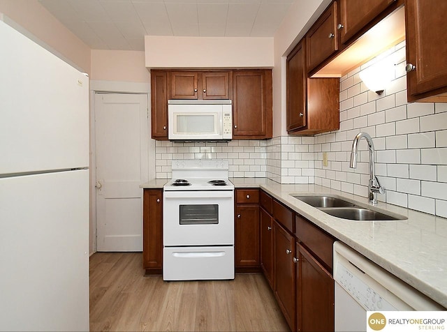 kitchen featuring sink, backsplash, light stone counters, light hardwood / wood-style floors, and white appliances