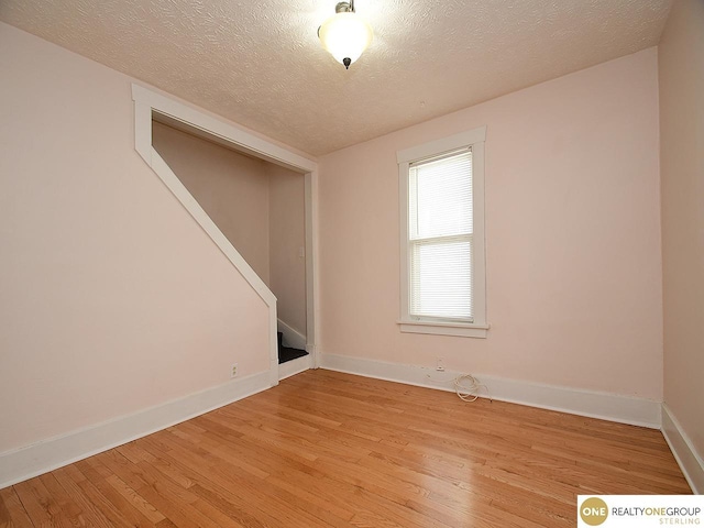 empty room with a textured ceiling and light hardwood / wood-style flooring