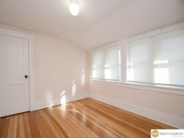 unfurnished room with lofted ceiling, hardwood / wood-style flooring, and a textured ceiling