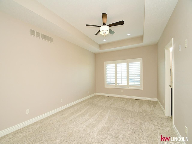 carpeted spare room featuring a raised ceiling and ceiling fan