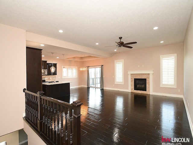 living room with sink, dark wood-type flooring, a tile fireplace, ceiling fan, and a textured ceiling