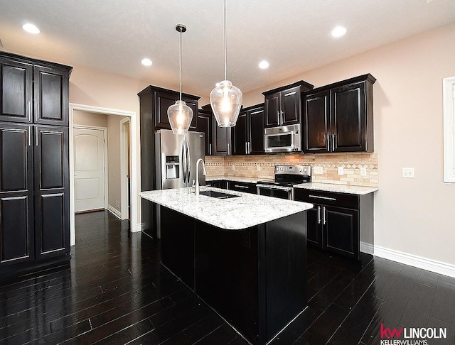 kitchen featuring pendant lighting, sink, stainless steel appliances, a center island with sink, and decorative backsplash