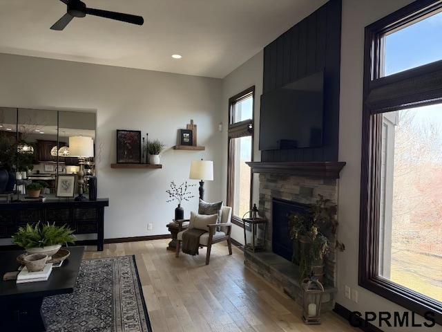 living area featuring hardwood / wood-style flooring, ceiling fan, a stone fireplace, and a wealth of natural light