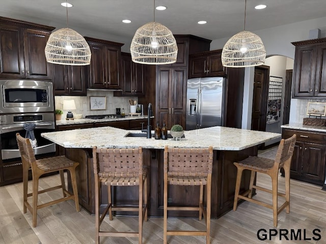 kitchen with pendant lighting, stainless steel appliances, an island with sink, and dark brown cabinets