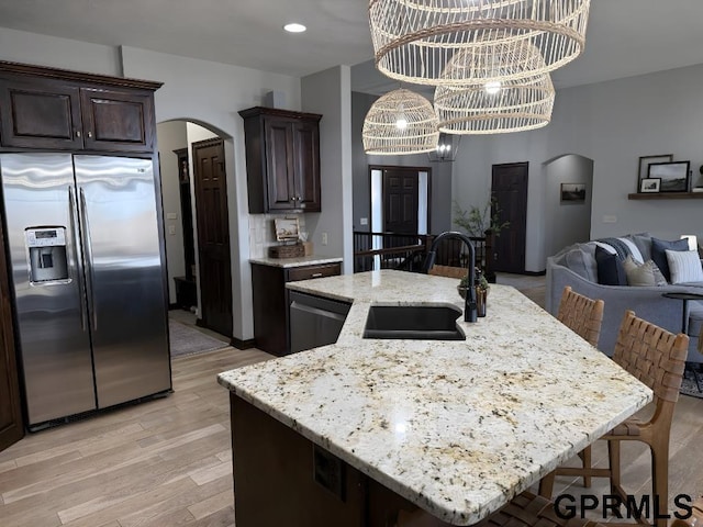 kitchen featuring appliances with stainless steel finishes, sink, dark brown cabinetry, a center island with sink, and an inviting chandelier