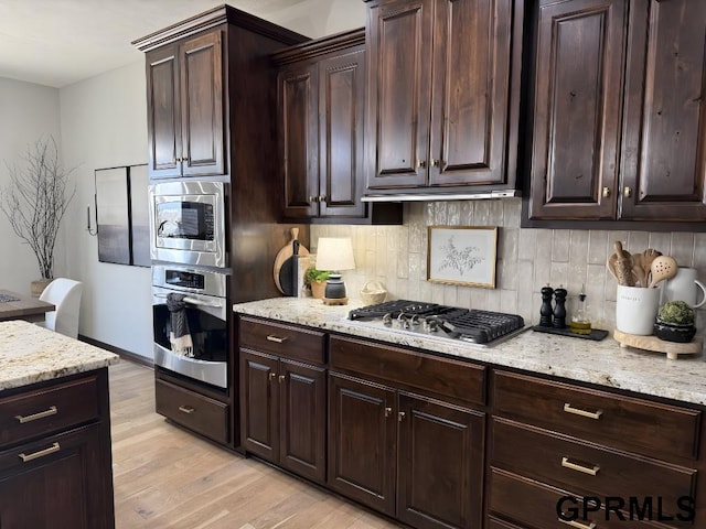 kitchen featuring light stone counters, dark brown cabinets, stainless steel appliances, and light hardwood / wood-style flooring