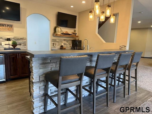 bar with dark brown cabinets, dark hardwood / wood-style flooring, hanging light fixtures, and decorative backsplash