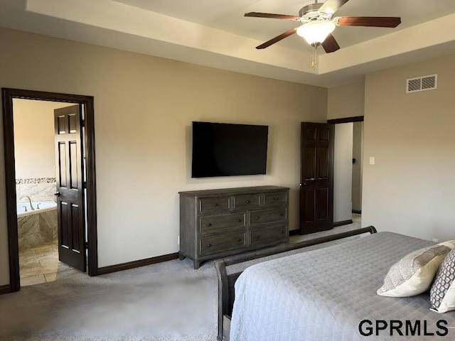 bedroom featuring a raised ceiling, ceiling fan, and ensuite bathroom