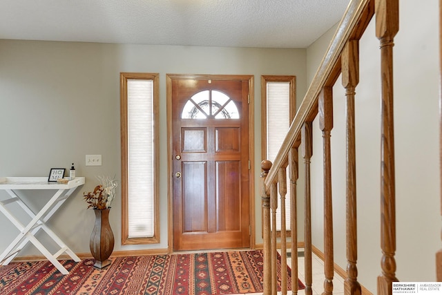 foyer with baseboards, stairway, and a textured ceiling