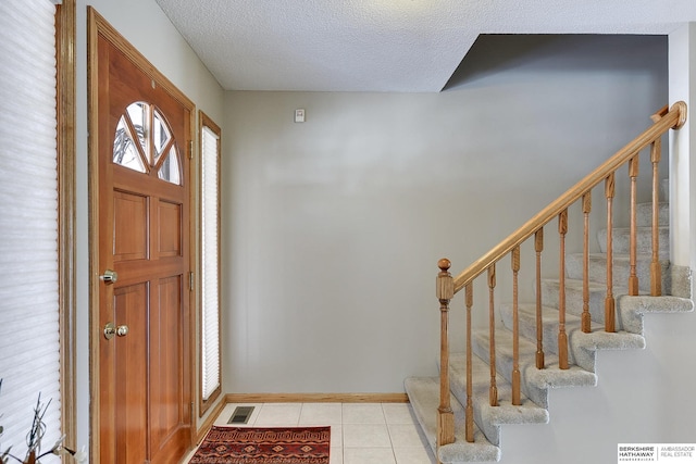 entrance foyer with light tile patterned floors, visible vents, stairway, a textured ceiling, and baseboards