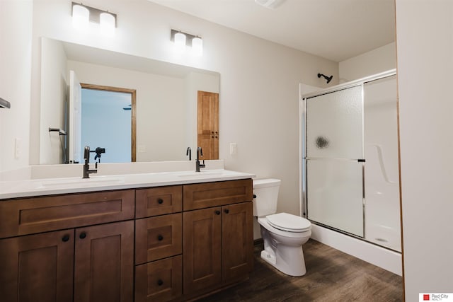 bathroom featuring wood-type flooring, toilet, vanity, and a shower with shower door